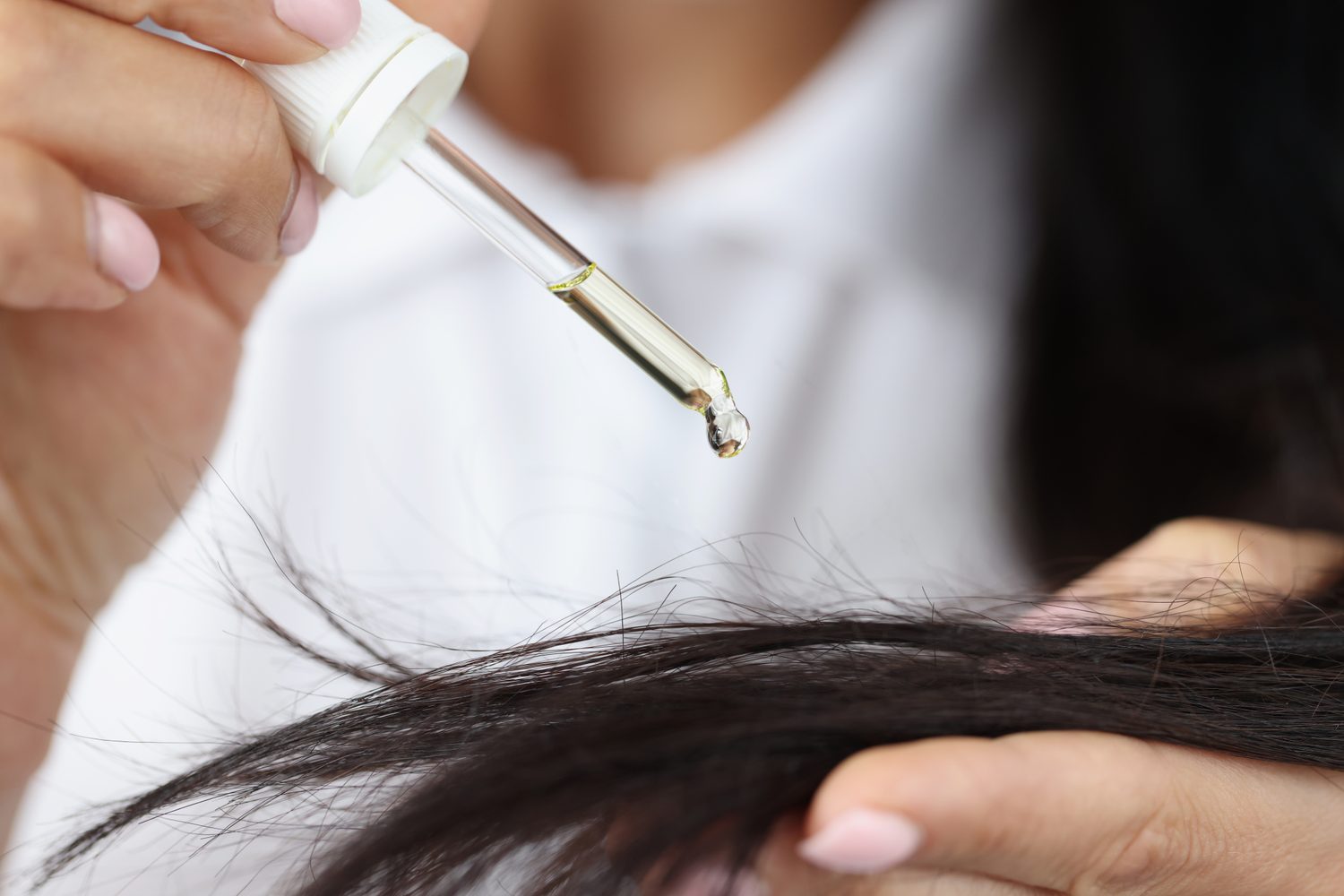 Femme appliquant délicatement de l’huile de ricin sur ses cheveux à l’aide de ses doigts.